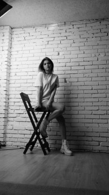Stüdyoda sandalyenin yanında uzun saçlı, siyah beyaz bir kadın poz veriyor..  