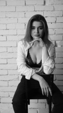 Beyaz tişörtlü, siyah beyaz saçlı, güzel ve seksi bir kadının stüdyoda beyaz bir duvara poz verdiği siyah beyaz bir fotoğraf..  