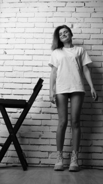 Stüdyoda sandalyenin yanında uzun saçlı, siyah beyaz bir kadın poz veriyor..  