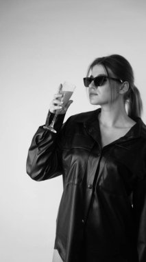 Siyah gömlekli ve güneş gözlüklü genç bir kadının stüdyoda poz verirken çekilmiş siyah beyaz bir fotoğrafı..  