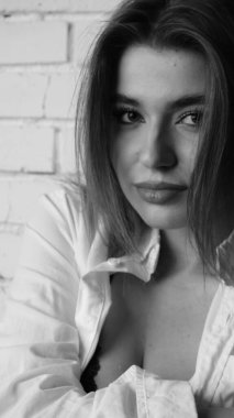 Beyaz tişörtlü, siyah beyaz saçlı, güzel ve seksi bir kadının stüdyoda beyaz bir duvara poz verdiği siyah beyaz bir fotoğraf..  