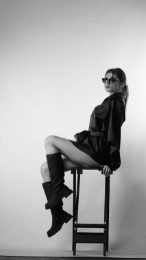 Siyah gömlekli ve güneş gözlüklü genç bir kadının stüdyoda poz verirken çekilmiş siyah beyaz bir fotoğrafı..  