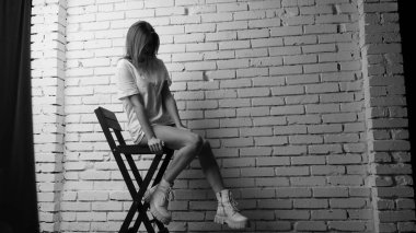 Stüdyoda sandalyenin yanında uzun saçlı, siyah beyaz bir kadın poz veriyor..  