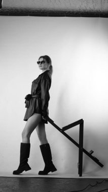 Siyah gömlekli ve güneş gözlüklü genç bir kadının stüdyoda poz verirken çekilmiş siyah beyaz bir fotoğrafı..  