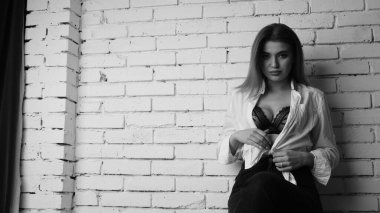 Beyaz tişörtlü, siyah beyaz saçlı, güzel ve seksi bir kadının stüdyoda beyaz bir duvara poz verdiği siyah beyaz bir fotoğraf..  