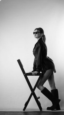 Siyah gömlekli ve güneş gözlüklü genç bir kadının stüdyoda poz verirken çekilmiş siyah beyaz bir fotoğrafı..  