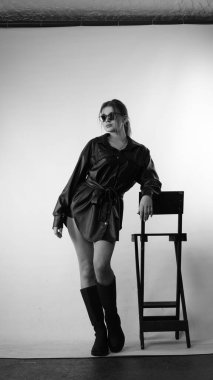 Siyah gömlekli ve güneş gözlüklü genç bir kadının stüdyoda poz verirken çekilmiş siyah beyaz bir fotoğrafı..  