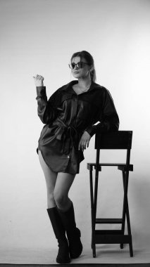 Siyah gömlekli ve güneş gözlüklü genç bir kadının stüdyoda poz verirken çekilmiş siyah beyaz bir fotoğrafı..  