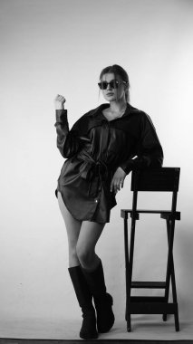 Siyah gömlekli ve güneş gözlüklü genç bir kadının stüdyoda poz verirken çekilmiş siyah beyaz bir fotoğrafı..  