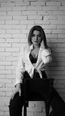 Beyaz tişörtlü, siyah beyaz saçlı, güzel ve seksi bir kadının stüdyoda beyaz bir duvara poz verdiği siyah beyaz bir fotoğraf..  