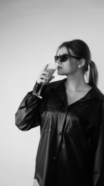 Siyah gömlekli ve güneş gözlüklü genç bir kadının stüdyoda poz verirken çekilmiş siyah beyaz bir fotoğrafı..  