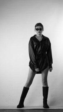 Siyah gömlekli ve güneş gözlüklü genç bir kadının stüdyoda poz verirken çekilmiş siyah beyaz bir fotoğrafı..  