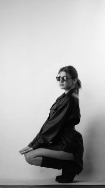 Siyah gömlekli ve güneş gözlüklü genç bir kadının stüdyoda poz verirken çekilmiş siyah beyaz bir fotoğrafı..  