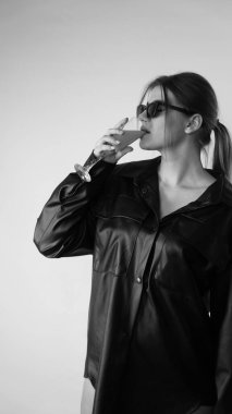 Siyah gömlekli ve güneş gözlüklü genç bir kadının stüdyoda poz verirken çekilmiş siyah beyaz bir fotoğrafı..  