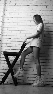 Stüdyoda sandalyenin yanında uzun saçlı, siyah beyaz bir kadın poz veriyor..  