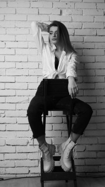 Beyaz tişörtlü, siyah beyaz saçlı, güzel ve seksi bir kadının stüdyoda beyaz bir duvara poz verdiği siyah beyaz bir fotoğraf..  