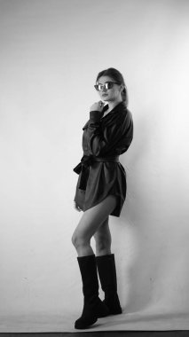 Siyah gömlekli ve güneş gözlüklü genç bir kadının stüdyoda poz verirken çekilmiş siyah beyaz bir fotoğrafı..  