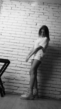 Stüdyoda sandalyenin yanında uzun saçlı, siyah beyaz bir kadın poz veriyor..  