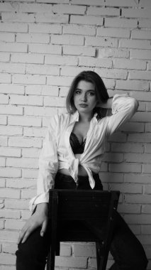 Beyaz tişörtlü, siyah beyaz saçlı, güzel ve seksi bir kadının stüdyoda beyaz bir duvara poz verdiği siyah beyaz bir fotoğraf..  