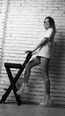 Stüdyoda sandalyenin yanında uzun saçlı, siyah beyaz bir kadın poz veriyor..  