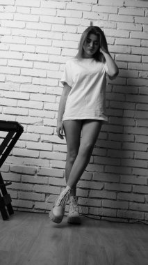 Stüdyoda sandalyenin yanında uzun saçlı, siyah beyaz bir kadın poz veriyor..  