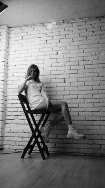 Stüdyoda sandalyenin yanında uzun saçlı, siyah beyaz bir kadın poz veriyor..  