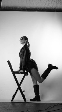 Siyah gömlekli ve güneş gözlüklü genç bir kadının stüdyoda poz verirken çekilmiş siyah beyaz bir fotoğrafı..  