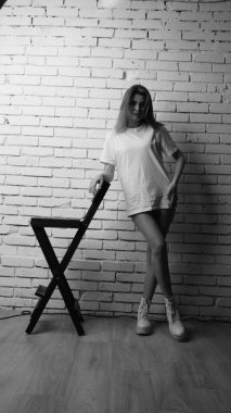 Stüdyoda sandalyenin yanında uzun saçlı, siyah beyaz bir kadın poz veriyor..  