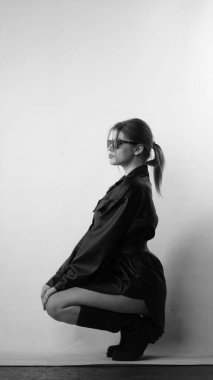 Siyah gömlekli ve güneş gözlüklü genç bir kadının stüdyoda poz verirken çekilmiş siyah beyaz bir fotoğrafı..  