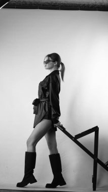 Siyah gömlekli ve güneş gözlüklü genç bir kadının stüdyoda poz verirken çekilmiş siyah beyaz bir fotoğrafı..  