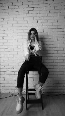 Beyaz tişörtlü, siyah beyaz saçlı, güzel ve seksi bir kadının stüdyoda beyaz bir duvara poz verdiği siyah beyaz bir fotoğraf..  