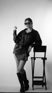 Siyah gömlekli ve güneş gözlüklü genç bir kadının stüdyoda poz verirken çekilmiş siyah beyaz bir fotoğrafı..  