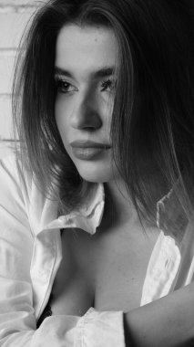 Beyaz tişörtlü, siyah beyaz saçlı, güzel ve seksi bir kadının stüdyoda beyaz bir duvara poz verdiği siyah beyaz bir fotoğraf..  