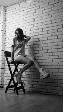 Stüdyoda sandalyenin yanında uzun saçlı, siyah beyaz bir kadın poz veriyor..  