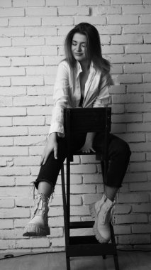 Beyaz tişörtlü, siyah beyaz saçlı, güzel ve seksi bir kadının stüdyoda beyaz bir duvara poz verdiği siyah beyaz bir fotoğraf..  