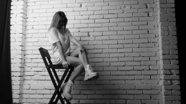 Stüdyoda sandalyenin yanında uzun saçlı, siyah beyaz bir kadın poz veriyor..  