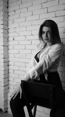 Beyaz tişörtlü, siyah beyaz saçlı, güzel ve seksi bir kadının stüdyoda beyaz bir duvara poz verdiği siyah beyaz bir fotoğraf..  