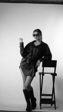 Siyah gömlekli ve güneş gözlüklü genç bir kadının stüdyoda poz verirken çekilmiş siyah beyaz bir fotoğrafı..  