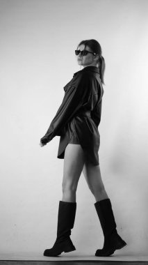 Siyah gömlekli ve güneş gözlüklü genç bir kadının stüdyoda poz verirken çekilmiş siyah beyaz bir fotoğrafı..  