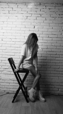 Stüdyoda sandalyenin yanında uzun saçlı, siyah beyaz bir kadın poz veriyor..  