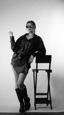 Siyah gömlekli ve güneş gözlüklü genç bir kadının stüdyoda poz verirken çekilmiş siyah beyaz bir fotoğrafı..  