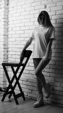 Stüdyoda sandalyenin yanında uzun saçlı, siyah beyaz bir kadın poz veriyor..  