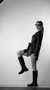 Siyah gömlekli ve güneş gözlüklü genç bir kadının stüdyoda poz verirken çekilmiş siyah beyaz bir fotoğrafı..  