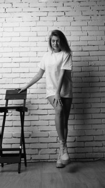 Stüdyoda sandalyenin yanında uzun saçlı, siyah beyaz bir kadın poz veriyor..  