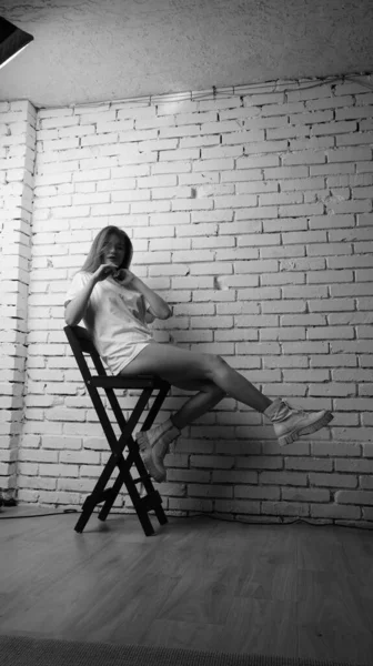 身穿T恤衫 留着长发的年轻漂亮女子站在演播室椅子旁边的黑白照片 — 图库照片