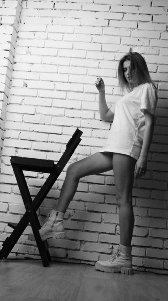 黒と白の写真若いです美しいです女性の長い髪はTシャツで身に着けています近くの椅子でポーズスタジオ — ストック写真