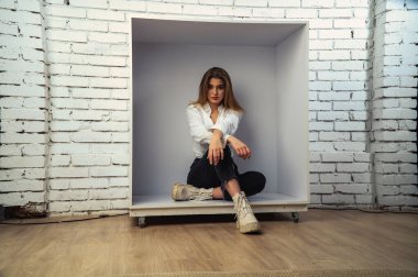 Stüdyoda beyaz gömlekli seksi ve seksi bir kadının beyaz bir duvara poz verdiği bir fotoğraf..  