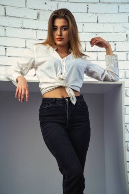 Stüdyoda beyaz gömlekli seksi ve seksi bir kadının beyaz bir duvara poz verdiği bir fotoğraf..  