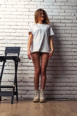 Stüdyoda beyaz bir duvara poz veren uzun saçlı seksi ve şehvetli genç bir kadının fotoğrafı..  