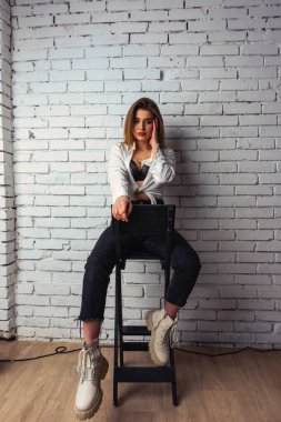 Stüdyoda beyaz gömlekli seksi ve seksi bir kadının beyaz bir duvara poz verdiği bir fotoğraf..  